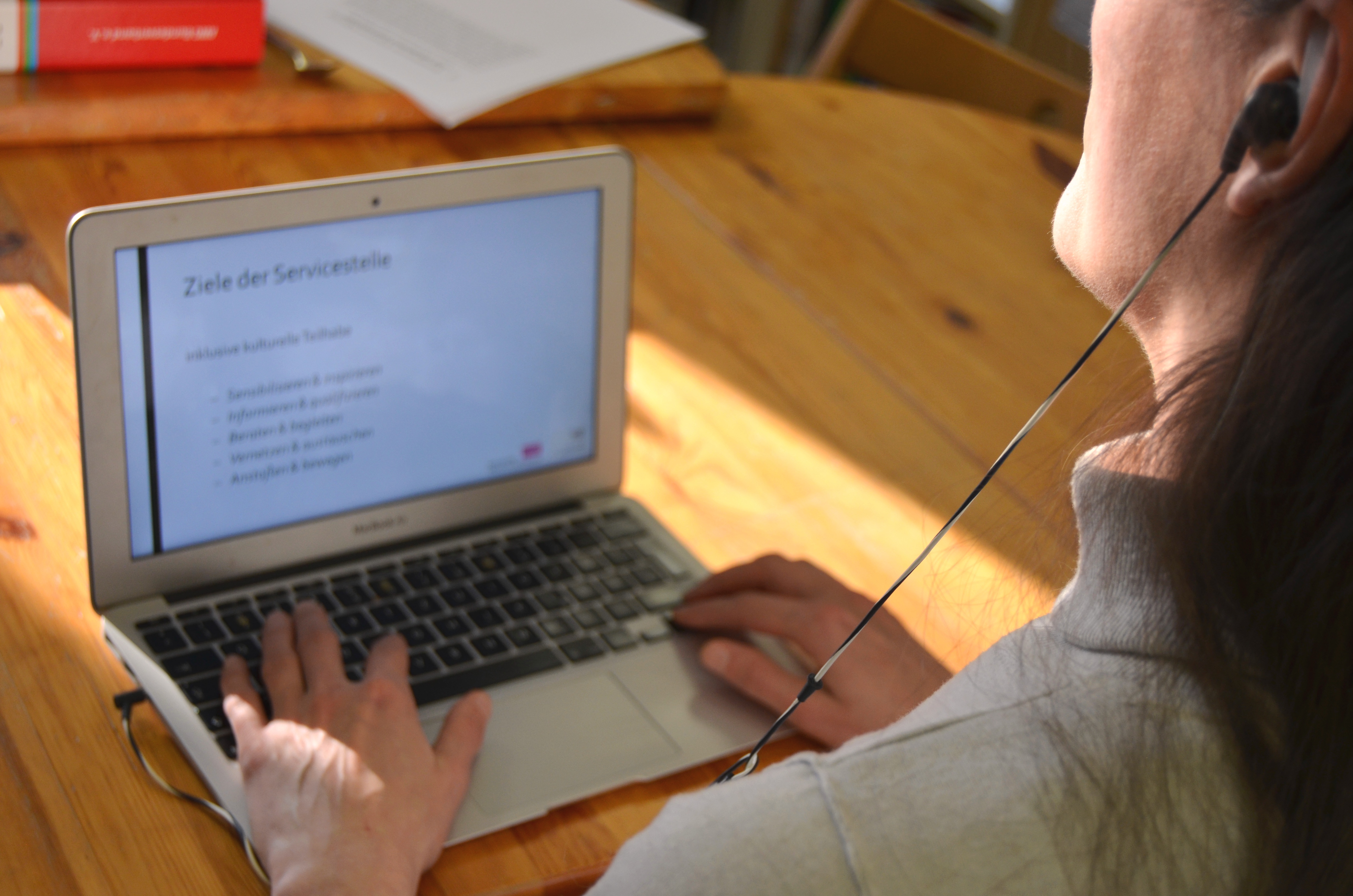 Zwei Hände auf einem Laptop. An den Laptop sind Kopfhörer angeschlossen, die die Person am Laptop im Ohr hat.