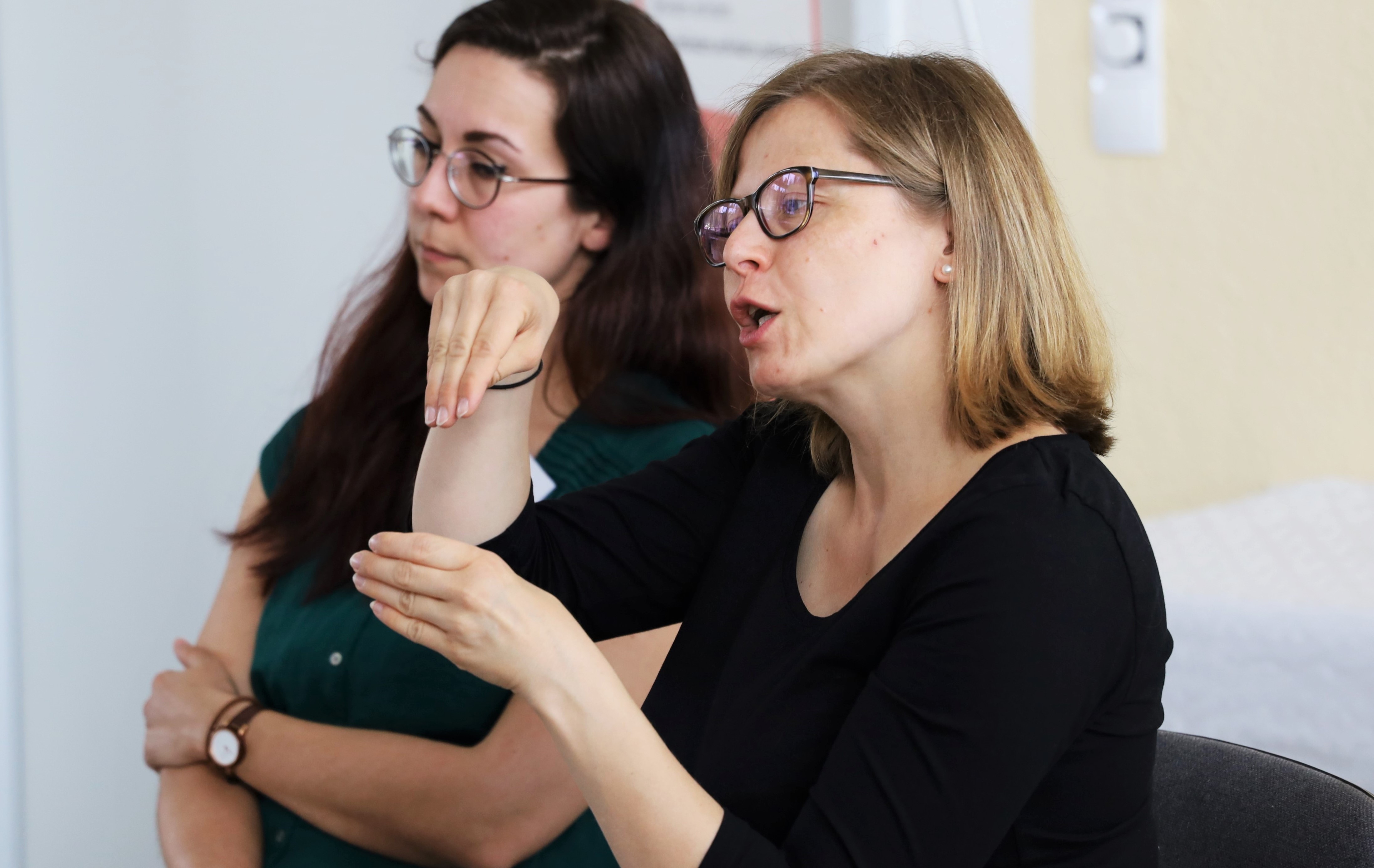 Zwei Gebärdensparchdolmetscherinnen sitzend. Eine der beiden übersetzt in Gebärdensprache.