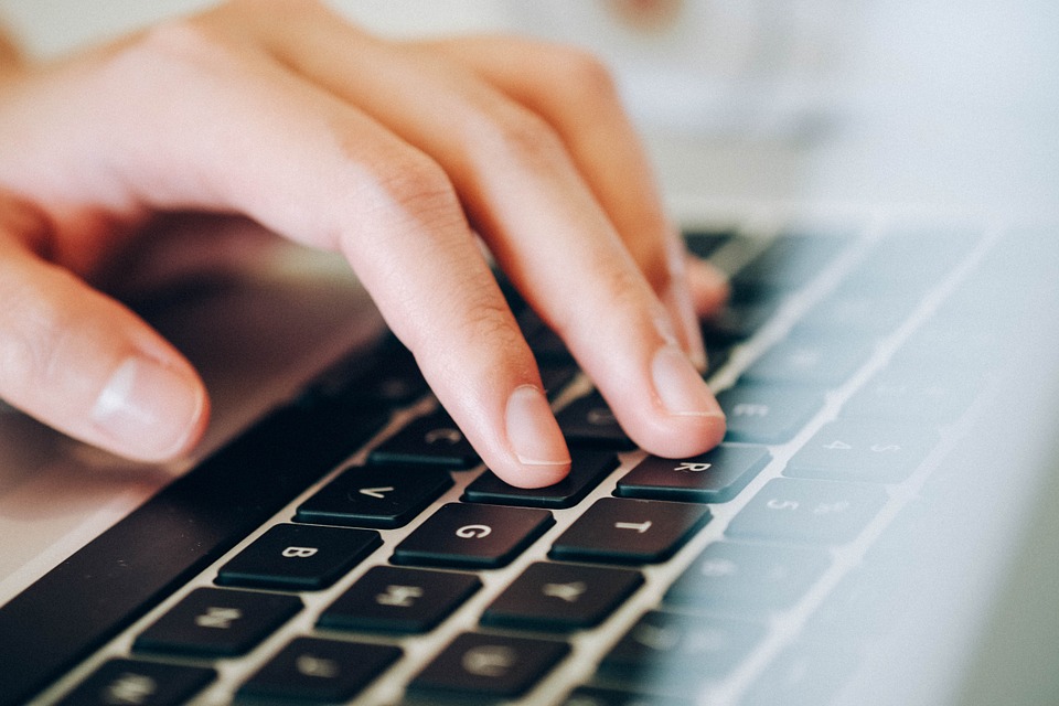 Das Foto zeigt die Tastatur eines Laptops. Eine Hand tippt auf die Tasten.