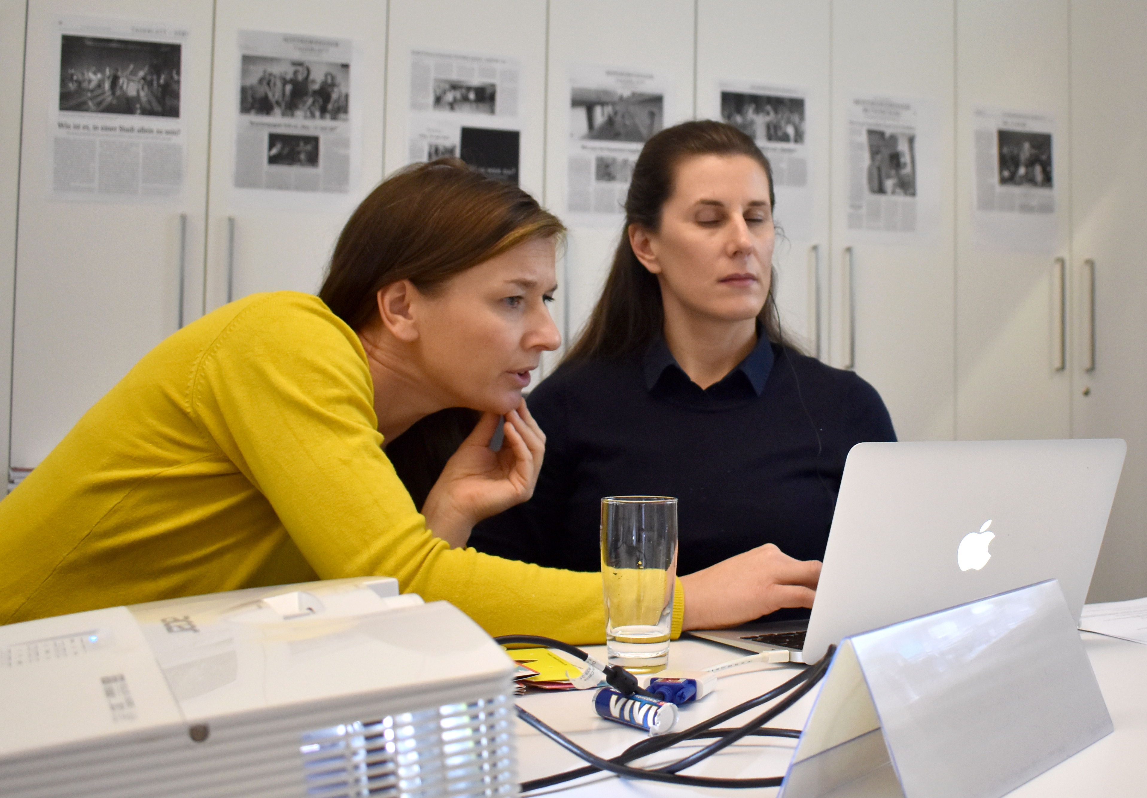 Das Foto zeigt zwei nebeneinandersitzende Personen vor einem Laptop. Workshops. Im Vordergrund steht ein Beamer.