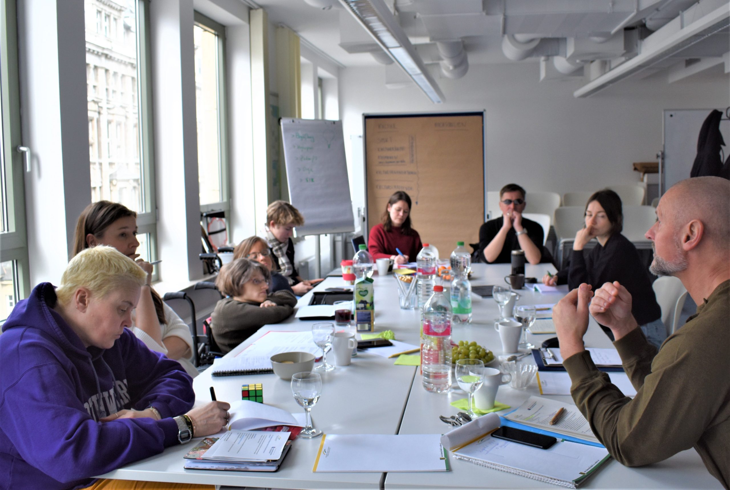 Das Foto zeigt einen langen Tisch. Um den Tisch herum sitzen in U-Form die Mitglieder des Runden Tisches