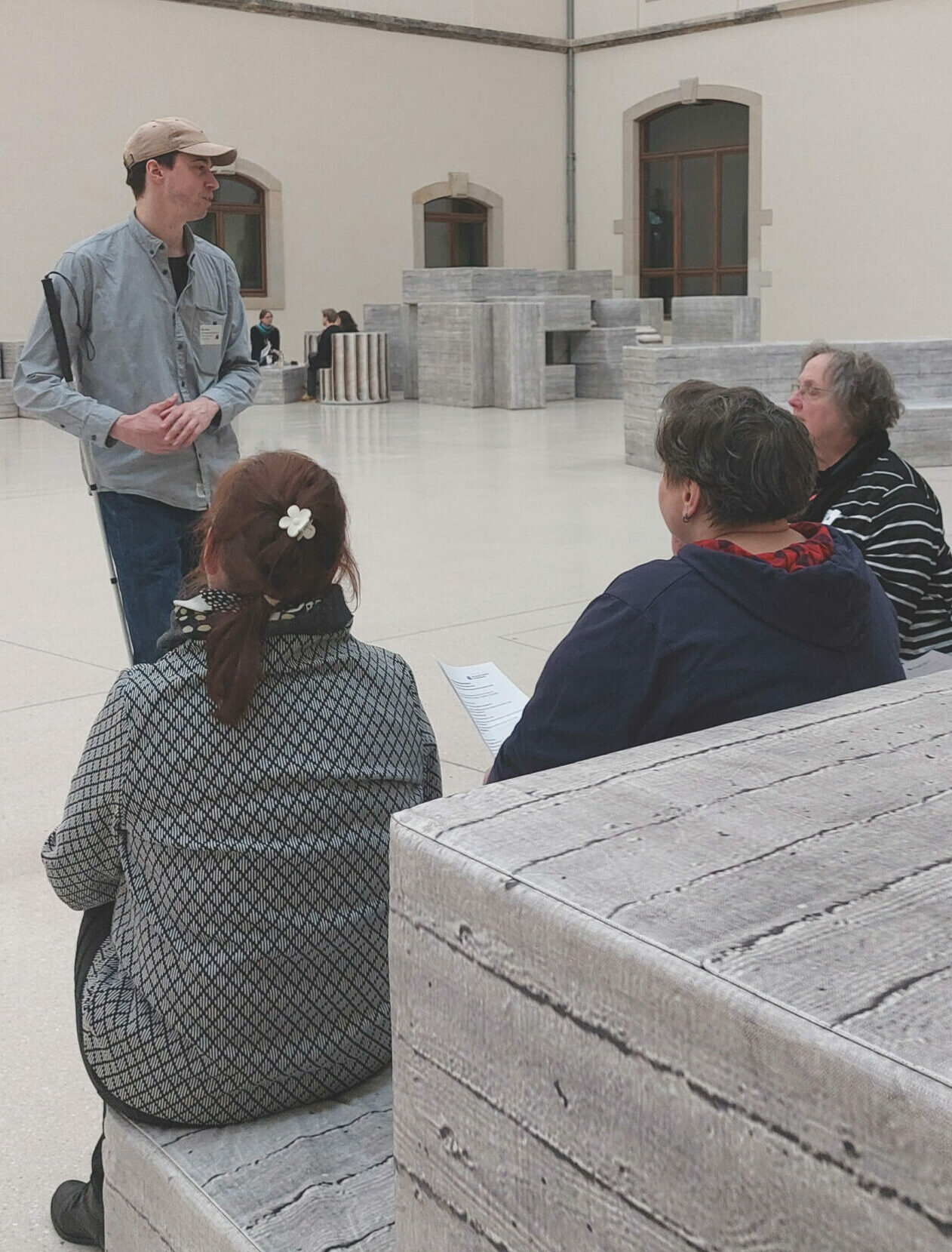 Situation einer Schulung im Saal eines Museums. Auf einer blockartigen Eckbank sitzen vier Seminarteilnehmer vor dem stehenden Referenten.