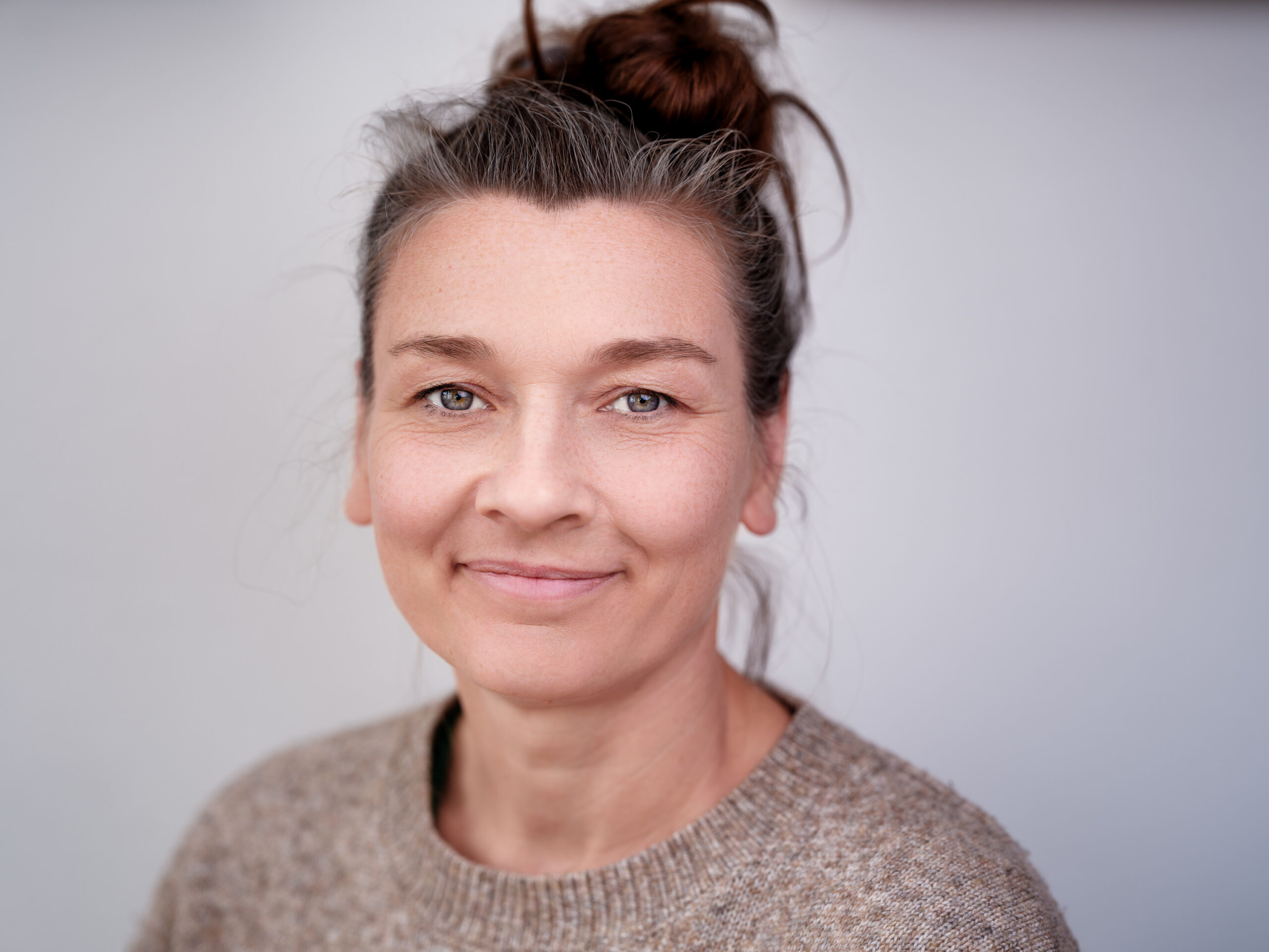 Johanna von der Waydbrink mit dunkelbraunen, locker hochgesteckten Haaren trägt einen beigefarbenen Strickpullover. Im Hintergrund ist eine neutrale, hellgraue Wand zu sehen.